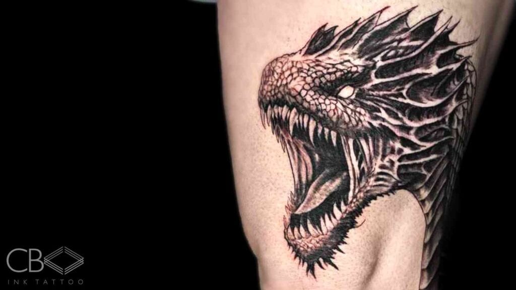 Spicy Ink The Coolest (and Most Painful) Tattoos You Can Get Raurie Tattoo Artist Realism Black and Grey Roaring Detailed Dragon Distinctive Teeth Leg Tattoo Blog Cover Image