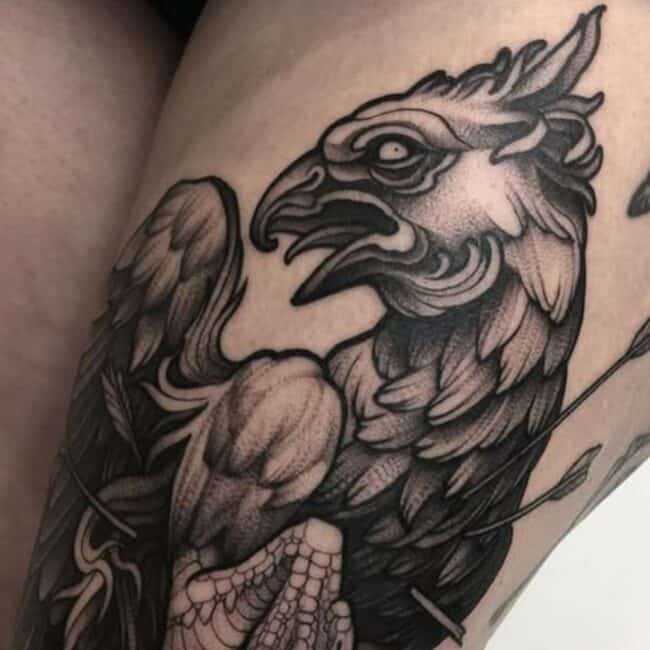Bold Blackwork Tattoo of a Griffin with Eagle and Lion Features Detailed Feathers and a Strong Muscle Sharp Claws Attacked by an Arrow Standout Design Leg Tattoo