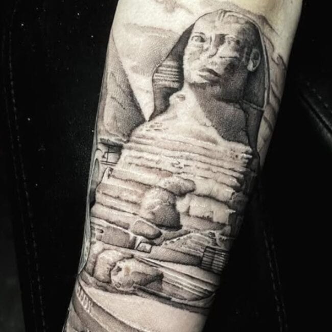 Black and Grey Realism Sphinx Ancient Egyptian Symbol Khafre Human Head Detailed Eyes Nose Ears Camels Desert Stones Pyramid Arm Forearm Tattoo